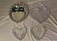 Top view of four heart-shaped candy dishes: ornate metal, pressed glass with roses, cut glass chevron, cut glass starburst