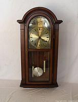 Full view of wooden wall clock showing dial, pendulum, and weights