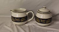 Creamer and lidded sugar bowl showing Tetley Teas blue band and gold scrollwork