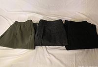 Three folded pairs of dress pants in olive green, charcoal heather, black