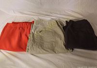 Three folded pants: red-orange, beige, dark brown