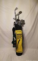 Complete set of clubs inserted in yellow and black carry bag, view of bag pockets and club heads