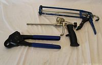 PEX crimper, caulking gun and spray foam gun displayed side by side