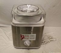 Front view of Cuisinart ICE-30BCC ice cream maker showing stainless steel exterior, clear lid, control knob, attached power cord