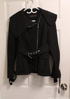 Front view of black ZARA Woman jacket on hanger showing overall design, collar, zipper, belt, cuffs