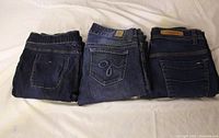 Three folded jeans showing back pockets and brand details