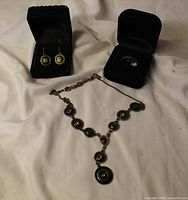 Necklace laid flat showing medallion design, earrings and ring each in black velvet boxes