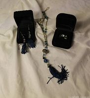 Necklace, earrings in display box, and ring in ring box laid out on fabric backdrop