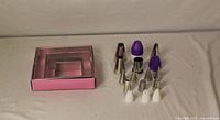 Square metal baking forms in pink box; assortment of piping nozzles and plastic couplers laid out