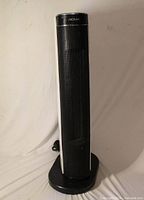 Front view of black and white Noma oscillating tower space heater on base with cord