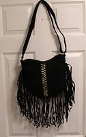 Front view of black fringe purse hanging, showing shape, strap, fringe, gold-tone chain