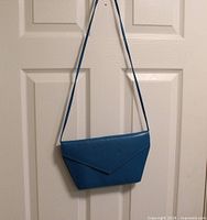 Full exterior view of blue Cabelli purse hanging to display shape, color and strap