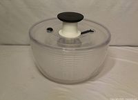 Overall view of the clear OXO salad spinner showing bowl, lid, and knob