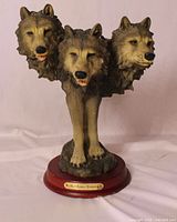 Front view of three-headed wolf sculpture showing full form and wood base