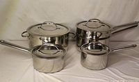 Five stainless steel pots and four lids displayed