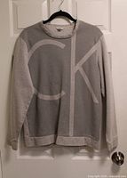 Front view of grey Calvin Klein sweatshirt hanging on door showing CK graphic and overall condition