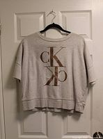 Front view of heather grey Calvin Klein short-sleeve sweatshirt with brown mirrored CK logo on hanger
