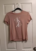 Front view of pink Calvin Klein t-shirt on hanger showing CK logo and overall condition