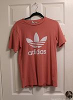 Front view of Adidas dusty-rose Trefoil T-shirt hanging on door