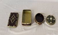 Rectangular and oval metal trinket boxes with lids open to show interiors and exterior jeweled decoration
