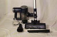 All vacuum components arranged on cloth backdrop including main body, wand, floor head, filter, charger, brush and crevice attachments