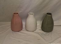 Front view of three ceramic vases in pink, white and olive