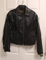 Front view of black leather fringe jacket hanging on door