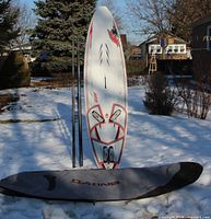 Board standing upright with fin installed, mast sections leaned alongside, Dakine bag on snow