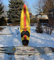 Full view of F2 yellow windsurf board standing vertically with Dakine bag on snow