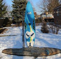 Full view of windsurf board, mast, and bag on snow