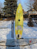 Full view of Seatrend Comp Wave 245 board standing upright with mast sections, fin and Dakine bag visible