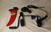 All four windsurfing components laid out: mast base, rig winch, harness line, red 28 cm fin