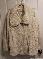 Full view of off-white Weatherproof faux sherpa coat hanging on door, showing collar, button, texture, and overall condition