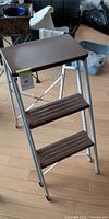 Front view of white metal folding ladder with three brown treads