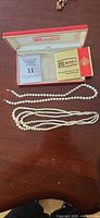 Open Majorica box with leaflet, single-strand necklace and triple-strand necklace laid out