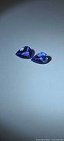 Two pear-cut violet-blue tanzanite stones on light background