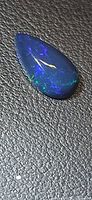 Pear-shaped black opal cabochon on textured background