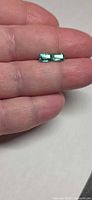 Pair of rectangular emerald-cut stones on fingertip for scale