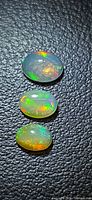 Three oval jelly opals on textured background, showing play-of-colour