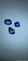 All three tanzanite gemstones arranged together on neutral background showing color and cut shapes
