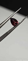 Pear-cut red spinel held in tweezers, side profile shows depth and clarity