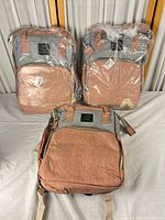 Front view of three LAND backpacks, two in plastic, one unwrapped