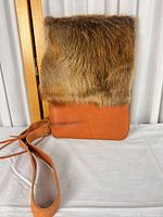 Front view showing tan leather body, brown fur flap, long strap