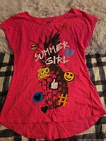 Front view of pink hi-lo top with pineapple and emoji graphics