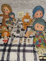 Overall view of six rag dolls, vintage photographs and orange tickets laid on bedspread