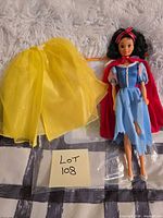 Doll with yellow overskirt, red cape and shoes laid out