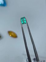 emerald-cut green gemstone in tweezers, frontal view
