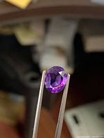 Oval purple amethyst held in tweezers, showing faceting and clarity