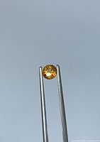 Front view of the round orange sapphire held in tweezers