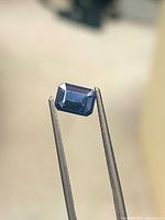 Front view of emerald-cut royal blue sapphire held by tweezers